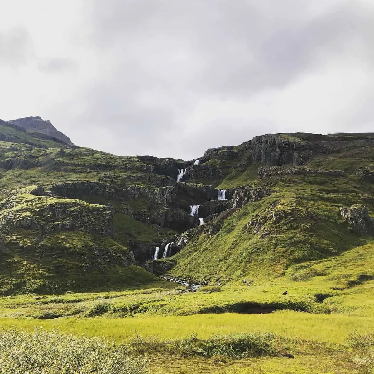 Fossar falla niður græna fjallshlíð í víðum dal.