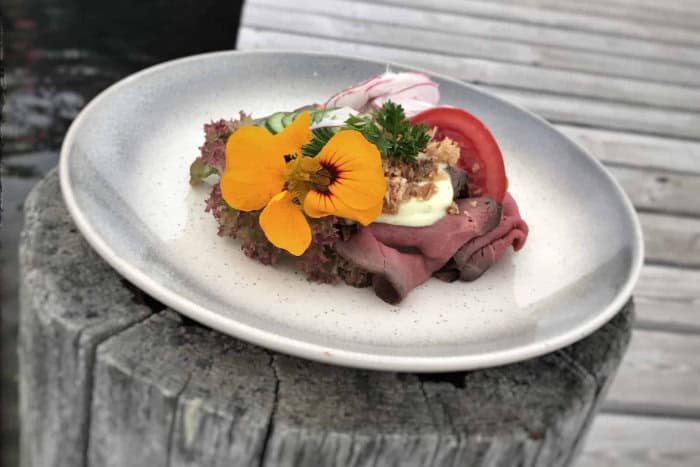 An open sandwich with sliced meat, vegetables and a flower garnish