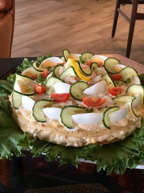 A savoury sandwich cake decorated with prawns, eggs and fresh vegetables.