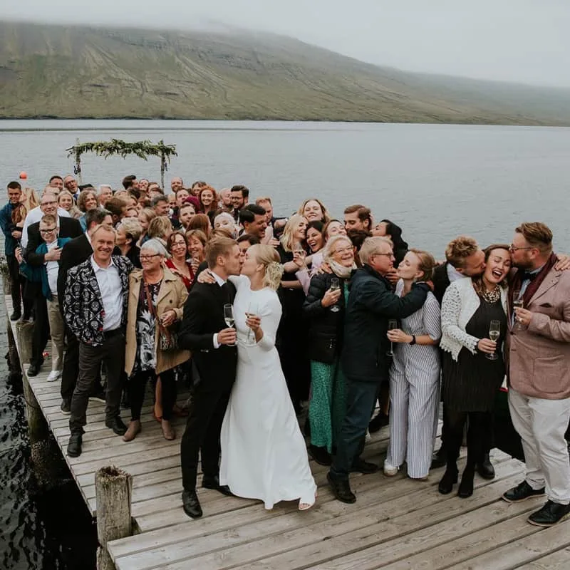 A wedding couple and their guests celebrating on a wooden pier by the fjord.